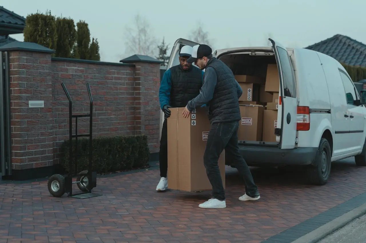 Deux déménageurs professionnels déchargeant un grand carton fragile d'un camion blanc
